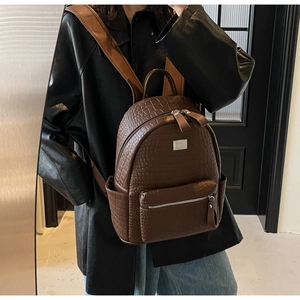 Detail of dark brown crocodile-embossed leather backpack with metal zipper and logo
