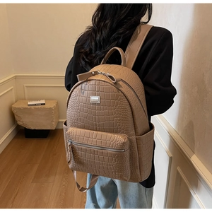 Detail showing brown crocodile-embossed leather texture and metal logo on a backpack