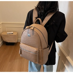 Detail view of khaki faux leather backpack with crocodile pattern and silver brand logo