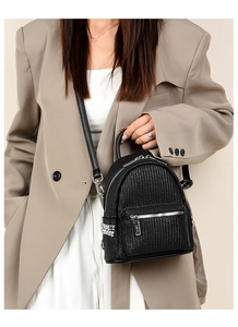 Detail of a black woven mini backpack for women featuring silver zippers and side rivets