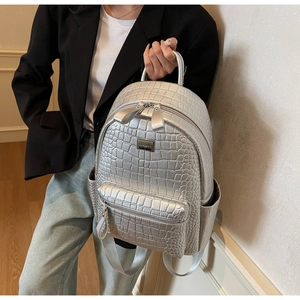 Detail of silver crocodile-textured backpack showing main zipper and front pocket