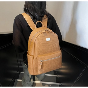 Detail of camel faux leather backpack featuring crocodile texture on minimalist background