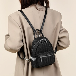 Minimalist black mini backpack with woven texture and silver studs on a model back