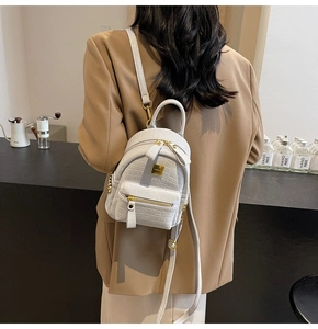 White faux leather mini backpack with stone texture shown on model in a cafe setting