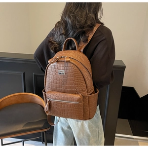 Detail of brown crocodile pattern backpack with silver metal logo plate on soft PU leather