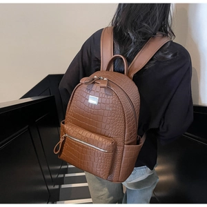 Detail view of brown crocodile texture leather backpack with metal logo and side pockets