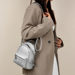 Detail of silver metallic woven mini backpack with side studs on model's back