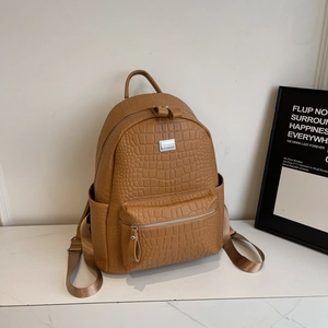 Detail of caramel brown faux crocodile leather backpack featuring silver logo and side pocket