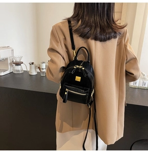 Detail of mini black backpack with crocodile texture and gold zippers worn over a blazer