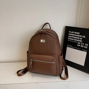 Detail of dark brown crocodile pattern leather texture and metal logo on backpack