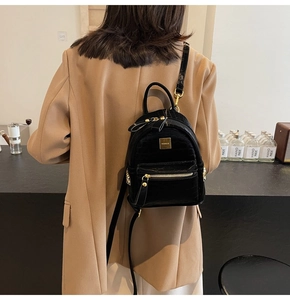 Mini black backpack with crocodile texture worn by model over a camel blazer
