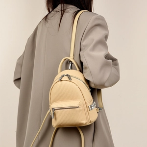 Detail of a beige mini backpack showing woven texture and silver metal side studs