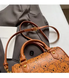 Close-up of brown barrel bag with bear prints and adjustable strap on a grey suit