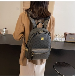 Detail view of black backpack with gray patterns, gold logo plate, and rivet accents