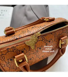 Detail of cute bear-shaped gold zipper on brown printed leather boston handbag