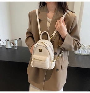 Mini cream faux crocodile leather backpack with gold hardware shown on a model in a cafe