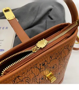 Close-up of golden bear-shaped zipper pull and printed bear pattern on brown leather bag