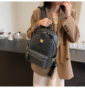 Detail view of black monogram backpack with gold metallic logo plate and chain decoration
