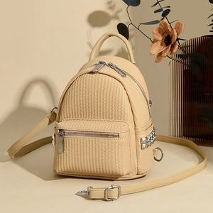 Detail of beige mini backpack featuring woven texture, silver studs, and a metal zipper logo