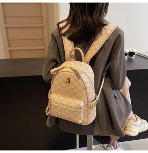 Detail of beige monogram backpack featuring golden zippers and a metal logo plaque