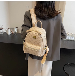 Detail showing the monogram pattern and gold logo plaque on beige backpack