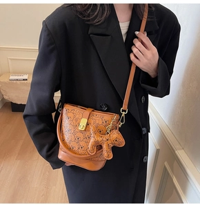 Brown bucket bag with bear print and dog charm shown worn with a black blazer jacket