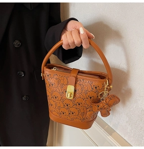 Brown bucket bag with cute bear prints featuring a gold twist lock and bear charm