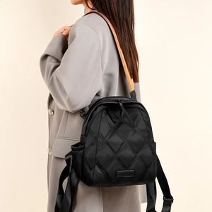 Detail of black quilted pattern backpack with logo tag and yellow edge handle