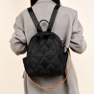 Detail of black quilted nylon backpack with metallic logo plate on grey blazer model