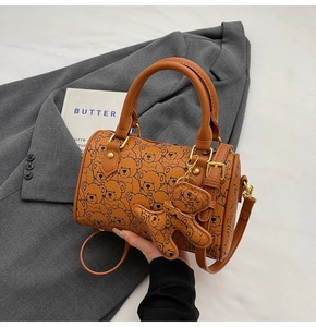 Close-up of brown barrel bag with bear print, textured leather, and matching bear charm