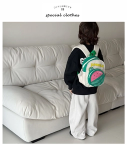 Detail of child wearing a white canvas dinosaur backpack with watermelon pocket design