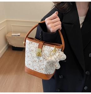 Detail view of stylish white bucket bag with bear print and brown leather handles