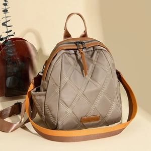Detail of quilted khaki backpack featuring leather trim and orange woven shoulder strap