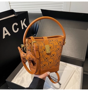 Detailed view of brown bucket bag with bear print, gold hardware and pendant in gift box
