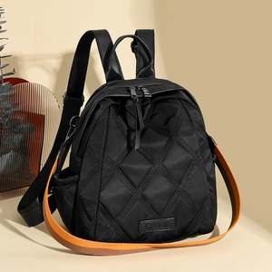 Close-up of black quilted nylon backpack with geometric diamond patterns and orange strap