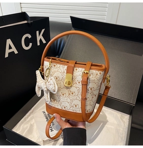 Detail of white bucket bag with bear print, brown handles, and elegant gold twist lock