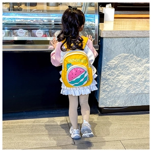 Kid's bright yellow backpack with watermelon print and dinosaur motif shown in use