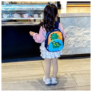 Rear view of a girl wearing a navy blue dinosaur backpack with orange pockets