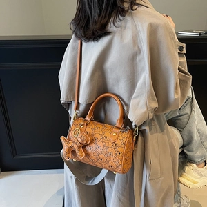 Brown leather barrel bag with cute bear print and charm, worn with a trench coat