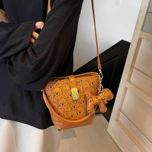 Brown bucket bag with bear print and bear charm worn on a female shoulder