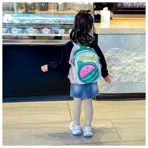 Kid's watermelon dinosaur backpack shown being worn by a child in a shop setting