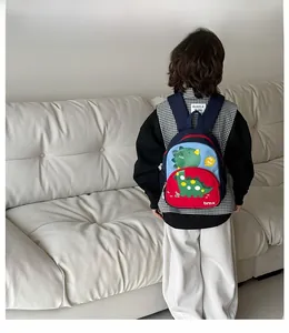 Rear view of a child wearing a colorful dinosaur backpack on a white fabric background