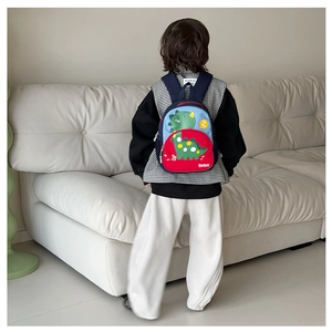 Rear view of a child wearing a blue and red color-block dinosaur backpack at home