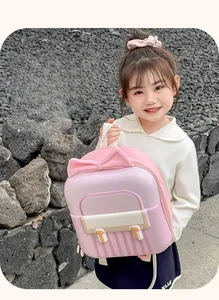 Pink school bag with 3D bow and hard shell texture held by a girl on rocky background