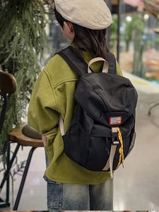 Side view of kid wearing a black nylon backpack with yellow cords and buckle detail