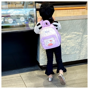Detail of children's purple backpack showing transparent PVC pocket with cartoon plush doll