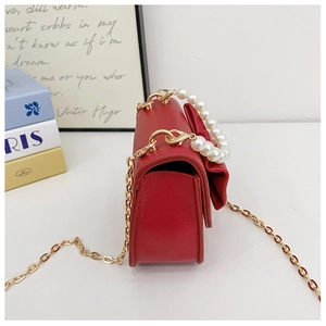 Side view of red girls crossbody bag with pearl handle, bow detail and chain strap