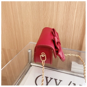 Detail of burgundy girl's crossbody bag with large bow and gold metal chain strap