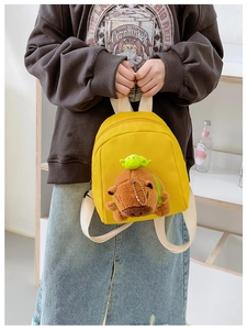 Close-up of a yellow canvas mini backpack with a cute plush Capybara pendant detail