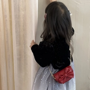 Girl wearing a stylish red crossbody bag with a large bow detail and gold chain strap
